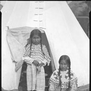 Cover image of Two unidentified girls standing in front of teepee