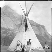 Cover image of Two people standing in front of tipi, Banff Indian Days Grounds