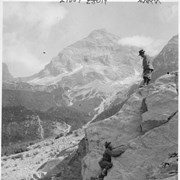 Cover image of Guide and tourist climbing a difficult rock face. Mt. Sir Donald in the distance / 27859